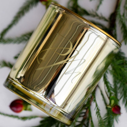 Gold candle holder with a decorative design on a white background with greenery