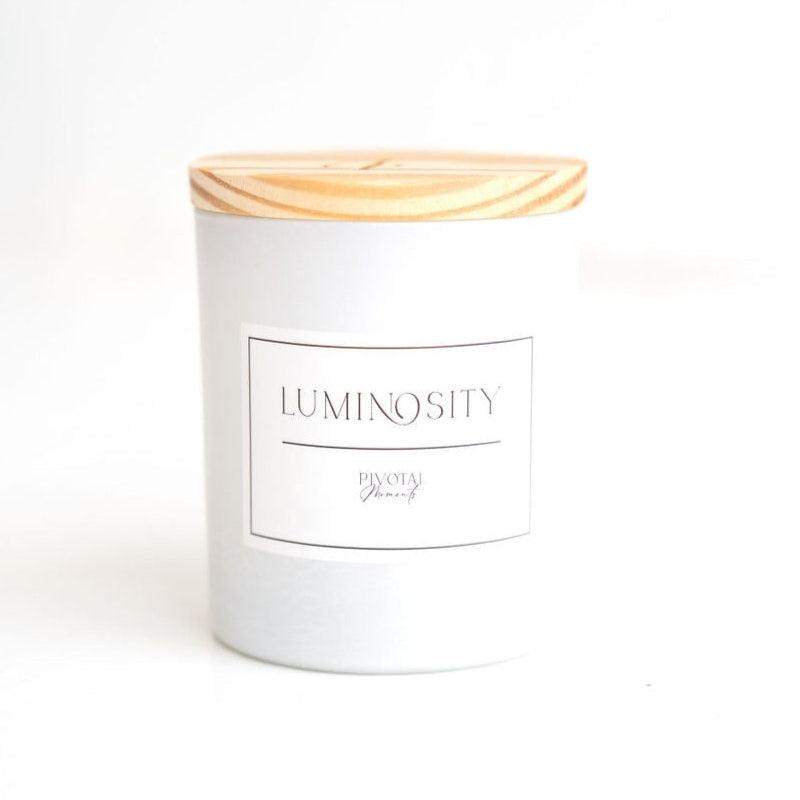A white cylindrical candle with a wooden lid, labeled 'LUMINOUS' and 'ORGANIC'.