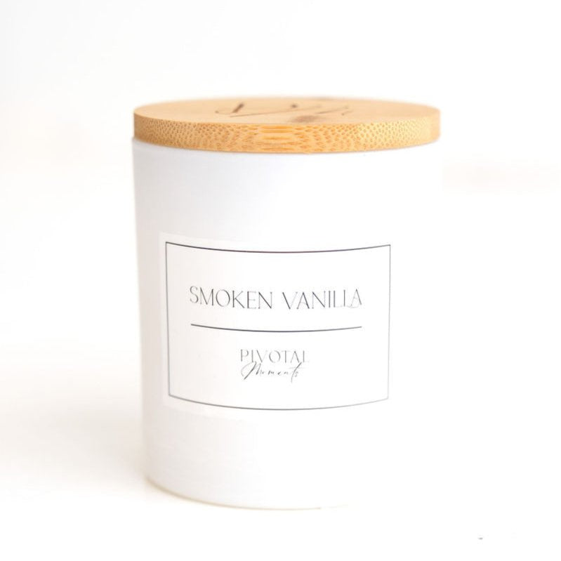 A white cylindrical candle with a wooden lid labeled 'SMOKEN VANILLA'.