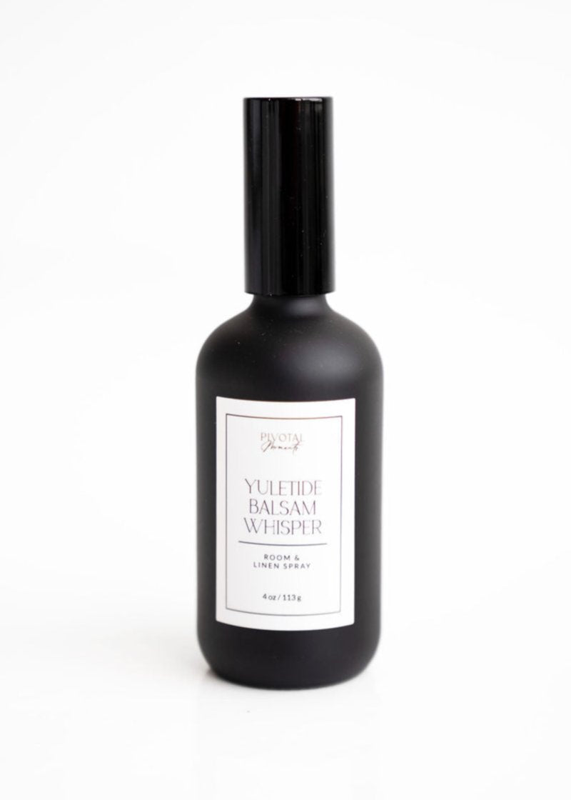 A black bottle of 'Yuletide Balsam Whisper' room and linen spray with a white label, showcasing the product name and volume.