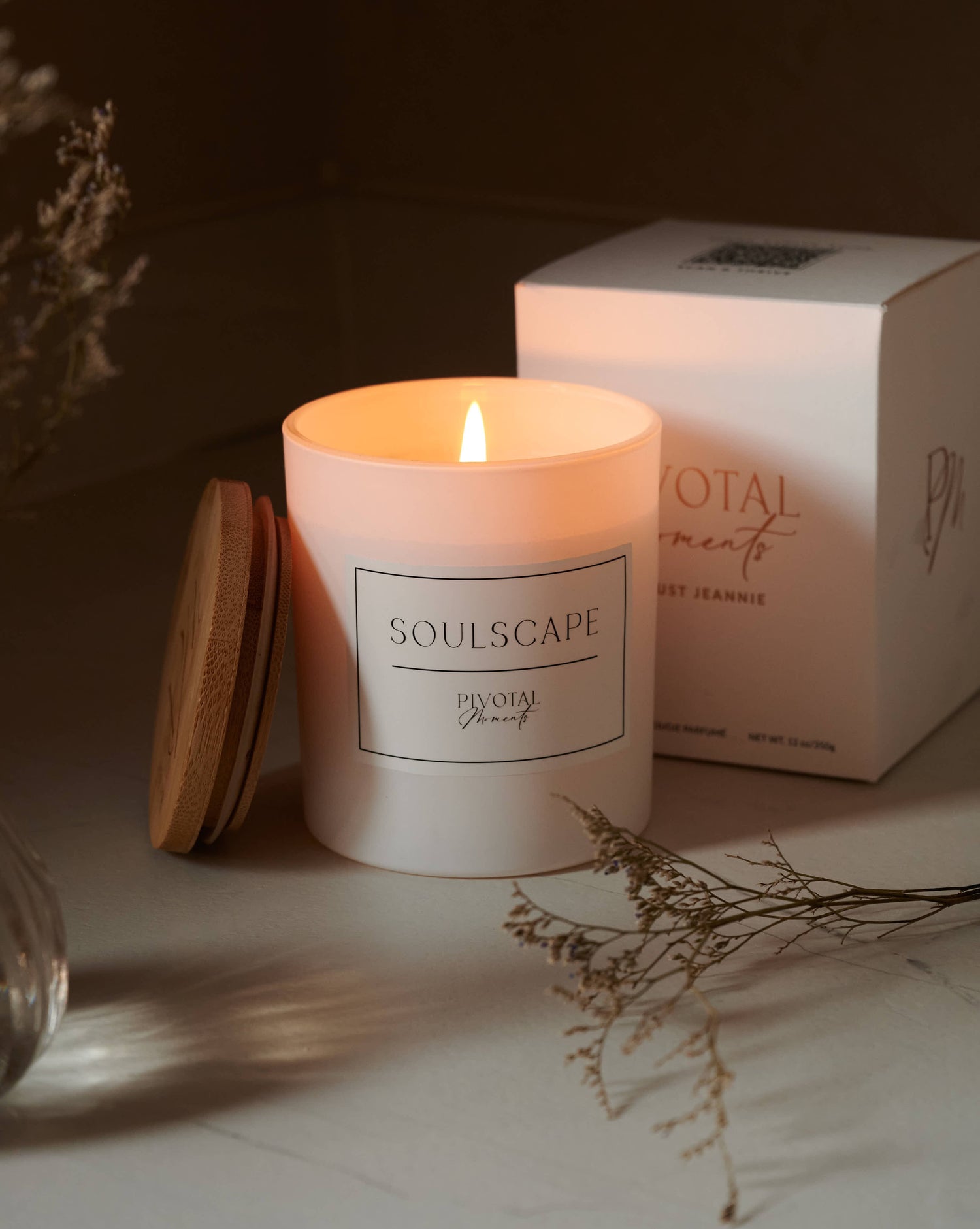 Lit candle with 'SOULSCAPE' branding next to a box on a surface.