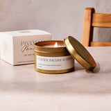 Candle in a gold tin with a white label on a light surface, with a box labeled 'Pivot' in the background.
