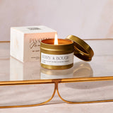 Lit candle in a gold tin with 'Pivotal' box in the background on a reflective surface.