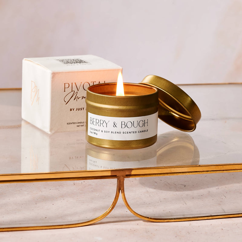 Lit candle in a gold tin with 'Pivotal' box in the background on a reflective surface.