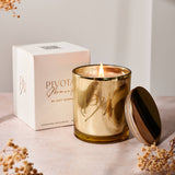 Gold candle with lid, white box, and dried flowers on a light surface