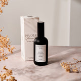 Black bottle with white label on a light surface with dried flowers and a white box in the background.