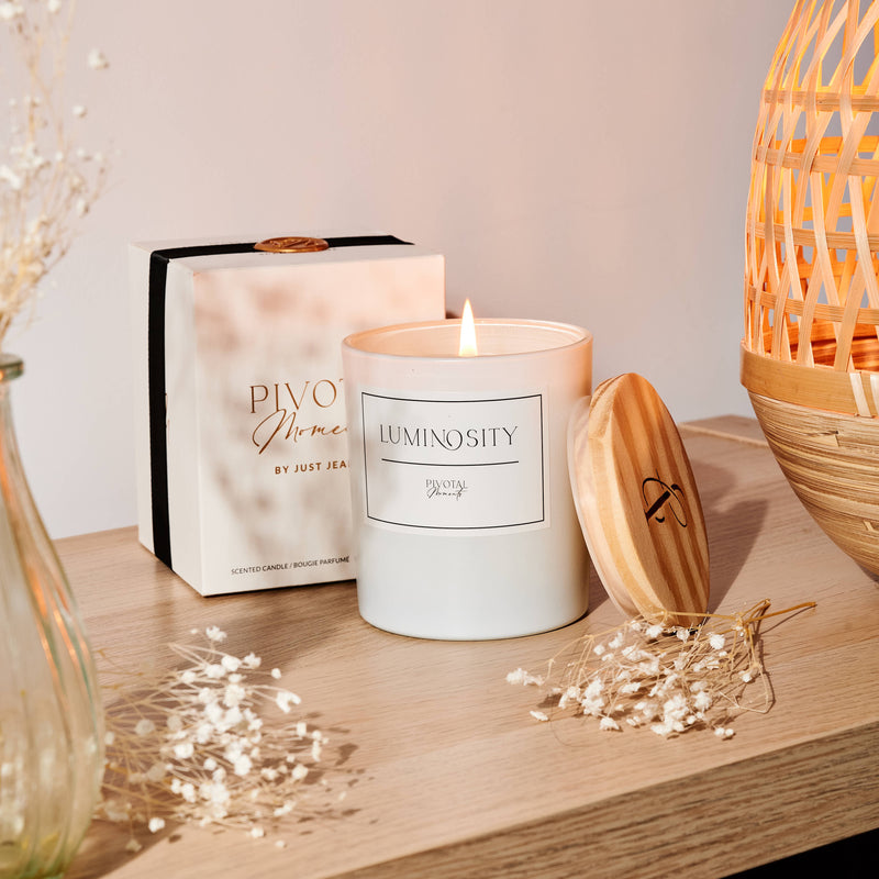 Candle with 'Luminosity' packaging on a wooden surface with decorative elements.