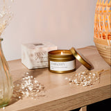 Lit candle in a decorative container on a wooden surface with a soft background