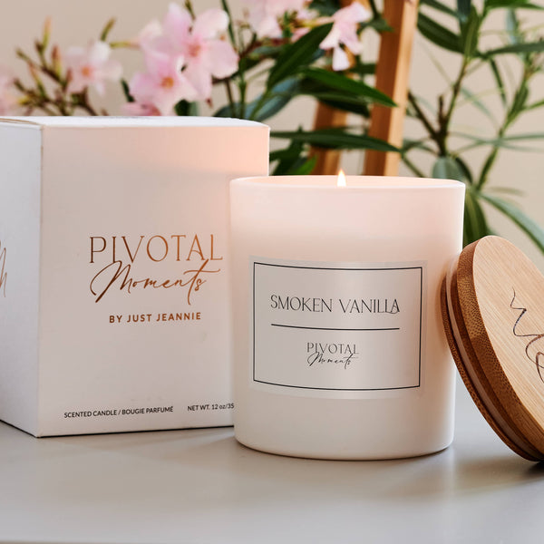 Pivotal Moments candle with packaging and wooden lid on a surface with flowers in the background
