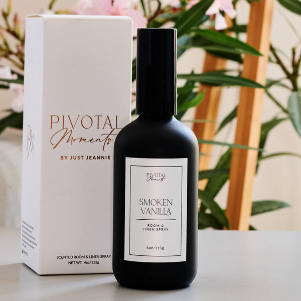Black bottle of 'Smoked Vanilla' room spray with packaging on a surface, floral background