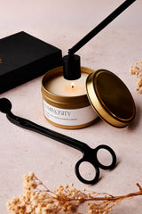 Candle with gold lid and 'Luminosity' label on a neutral background with a black snuffer