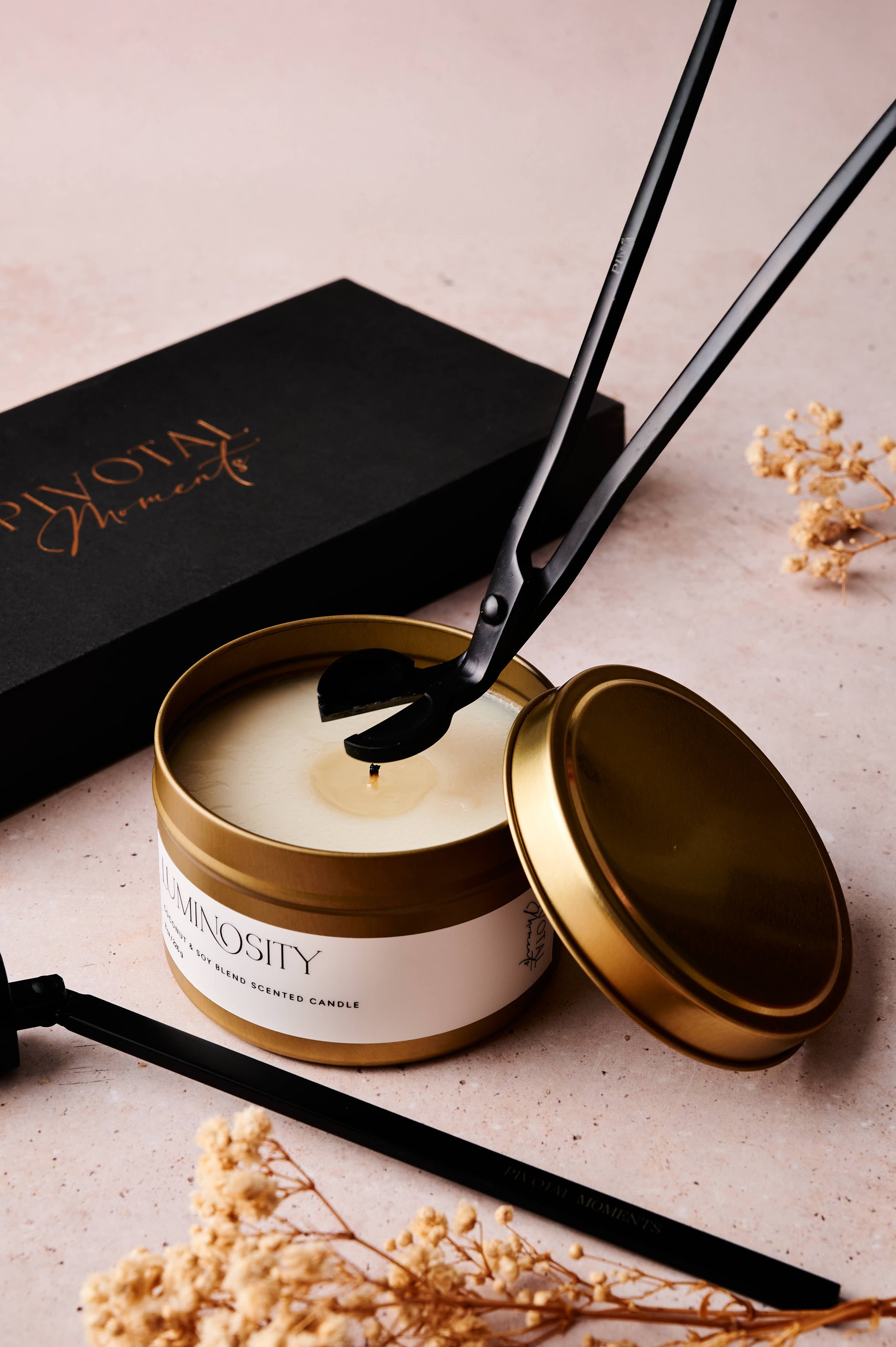Candle with gold lid and black wick  trimmeron a light surface with 'Pivotal Moments'vbranding.