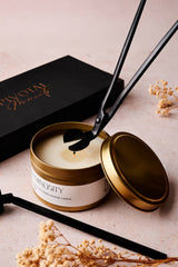 Candle with gold lid and black wick  trimmeron a light surface with 'Pivotal Moments'vbranding.